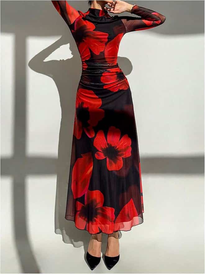 A person wearing a long-sleeved black dress with large red floral patterns stands against a white background, facing forward with arms raised.