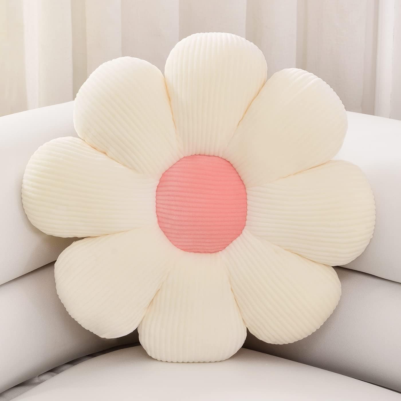 A white corduroy flower-shaped pillow with a pink center sits on a white sofa.