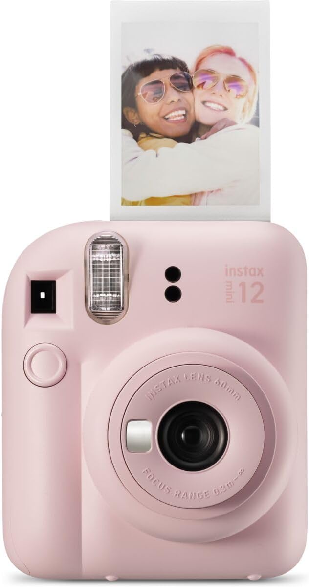 A pink instant camera prints a photo of two smiling people wearing sunglasses, hugging each other.