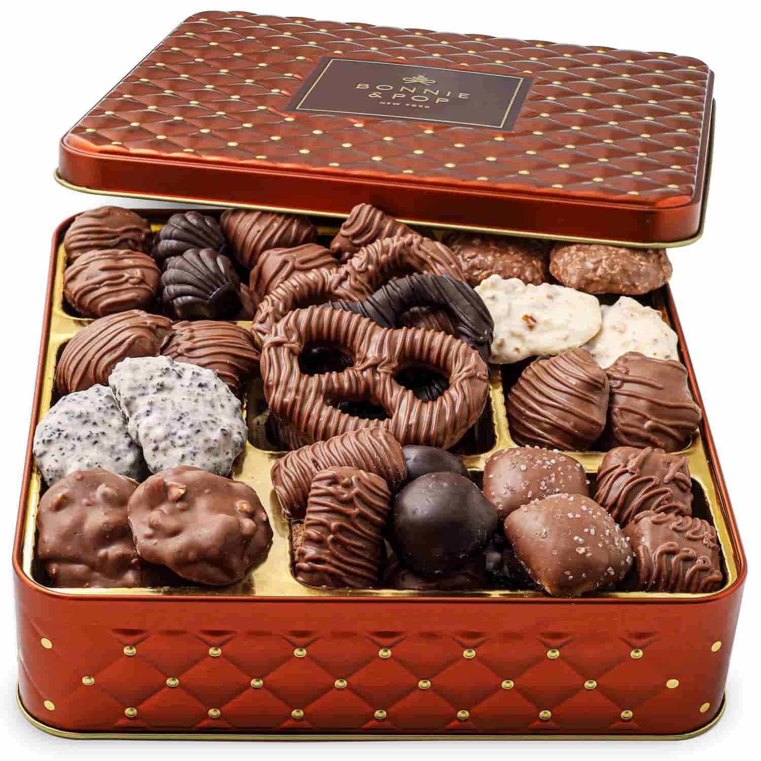 An open red tin box filled with assorted chocolate-covered cookies and treats, arranged neatly in rows.