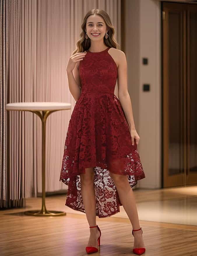 A woman stands indoors wearing a sleeveless, high-low red lace dress and matching red heels, smiling at the camera.