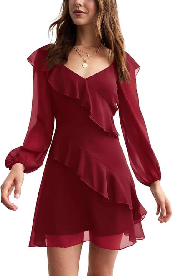 Woman wearing a long-sleeve, knee-length burgundy dress with ruffle details and layered chiffon fabric, accessorized with layered necklaces.