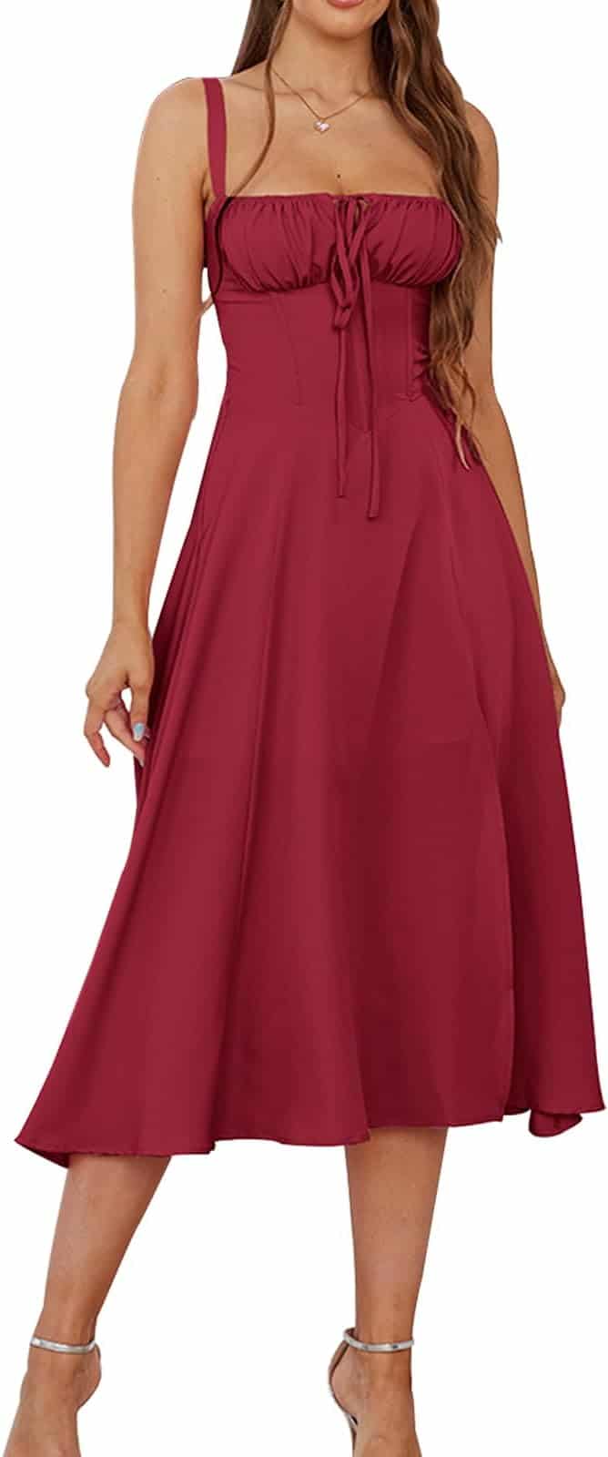 Woman wearing a sleeveless, midi-length, burgundy dress with a fitted bodice and tie detail at the bust, paired with strappy high-heeled sandals.