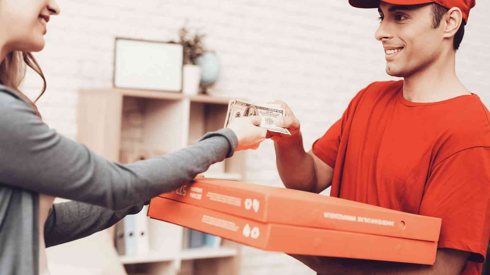 A person hands cash to a pizza delivery worker holding two pizza boxes.