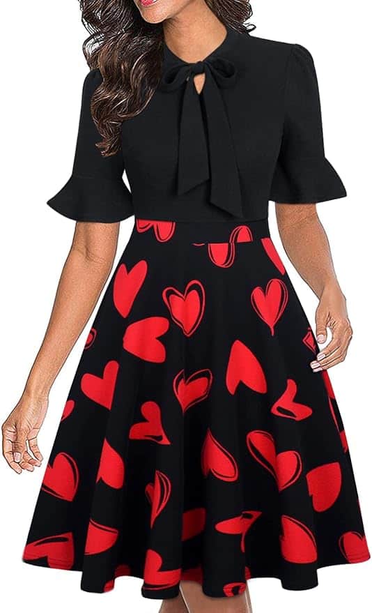 A woman wearing a black dress with short ruffled sleeves, a bow at the neckline, and a flared skirt patterned with red hearts.