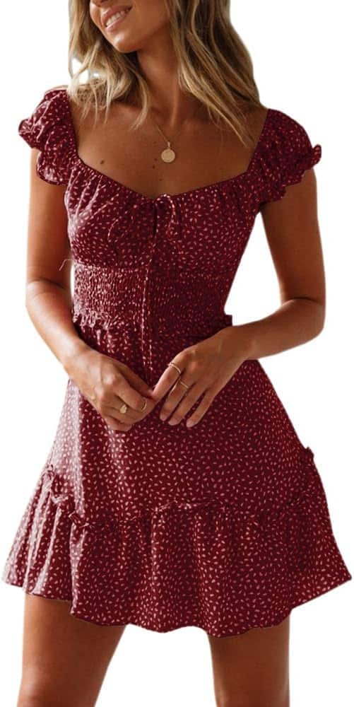 Woman wearing a short, red, floral-patterned dress with ruffled sleeves and hem, standing with hands clasped at her waist.