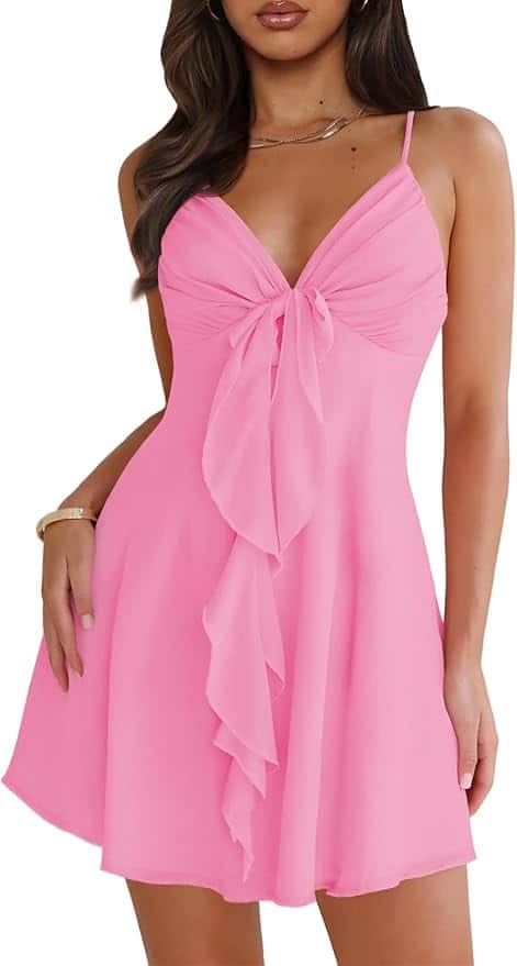 Woman wearing a sleeveless pink dress with thin straps, a front knot detail, and a ruffled accent down the center.