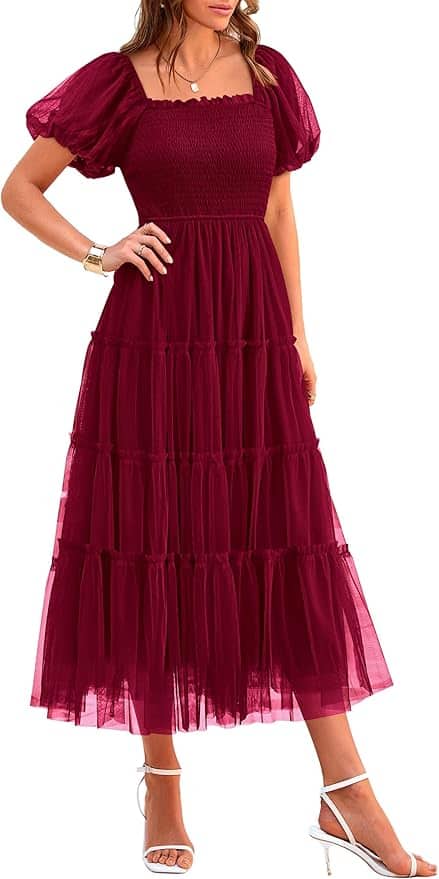 Woman wearing a burgundy, short-sleeve, square-neck, tiered tulle midi dress with white open-toe heels and a gold bracelet.