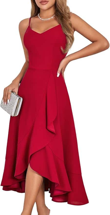 A woman wearing a sleeveless, red, asymmetrical midi dress holds a silver clutch and wears a necklace.