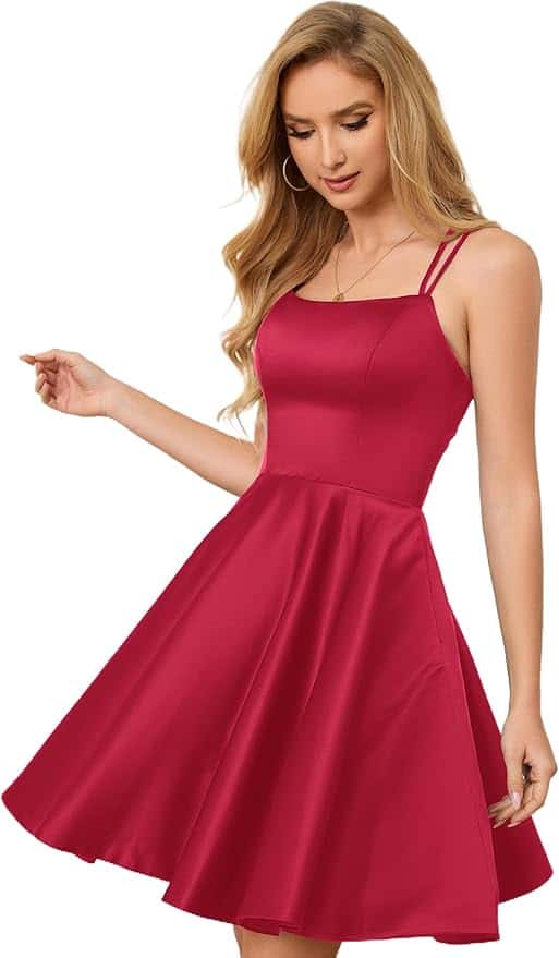 Woman wearing a sleeveless, fit-and-flare red dress with thin straps, standing and looking down with one arm slightly raised.