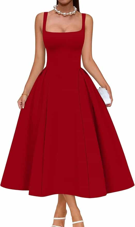 Woman wearing a sleeveless, square-neck, ankle-length red dress with a flared skirt, holding a small white clutch and wearing a pearl necklace and strappy heels.