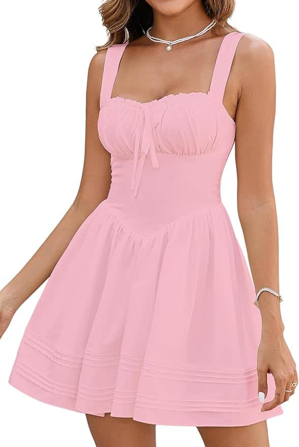 Woman wearing a sleeveless, light pink, knee-length dress with a fitted bodice, gathered bust, and flared skirt. She accessorizes with a necklace and bracelet.