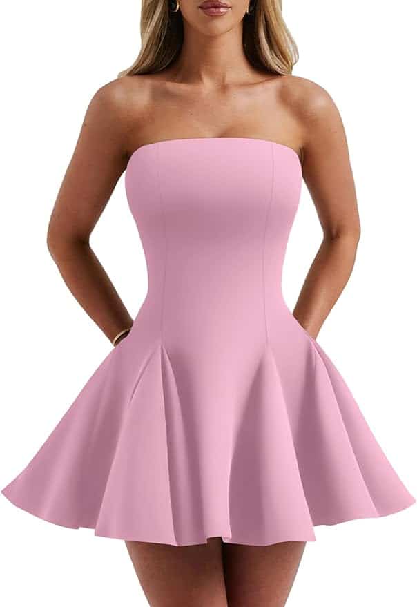 A woman wearing a strapless, light pink, A-line mini dress with side pockets, standing with her hands in the pockets.