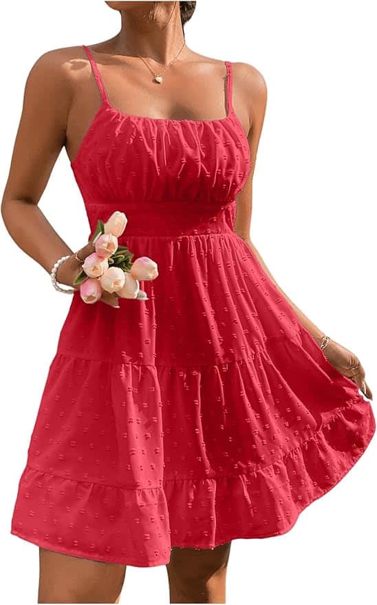 A woman wearing a sleeveless, tiered red sundress with spaghetti straps holds a small bouquet of pink flowers.