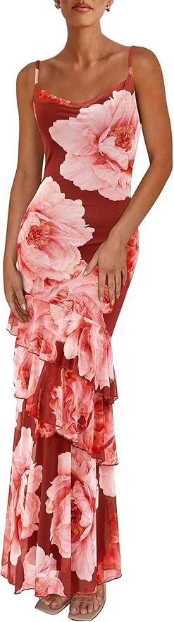 A woman wearing a sleeveless, fitted red dress with large pink floral prints and tiered ruffles at the bottom, standing in sandals.