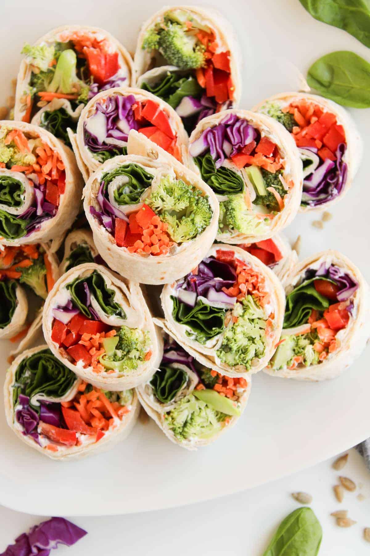 Sliced vegetable wraps arranged on a white plate, filled with spinach, broccoli, carrots, red cabbage, and red bell pepper.