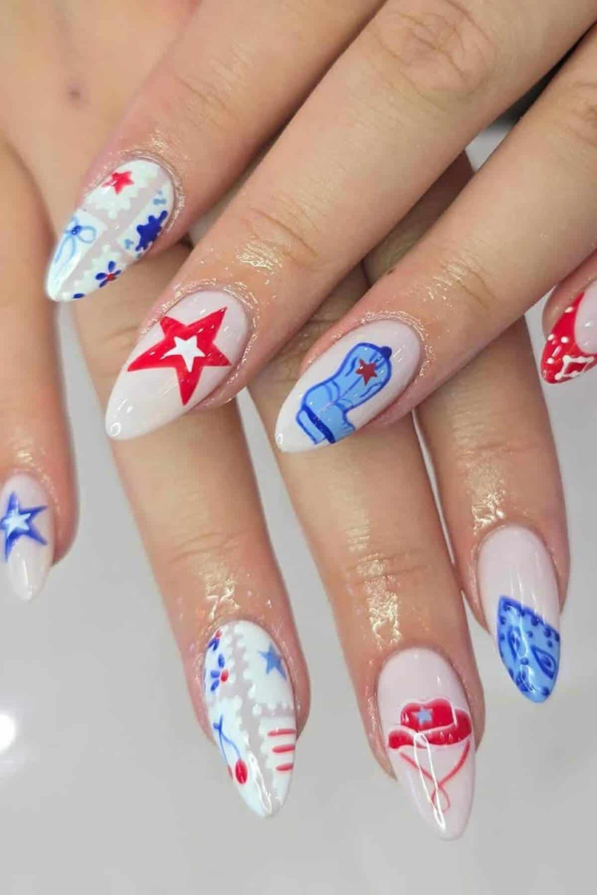 A hand with almond-shaped nails features white polish and red and blue Western-themed designs, including stars, boots, bandanas, and hats.