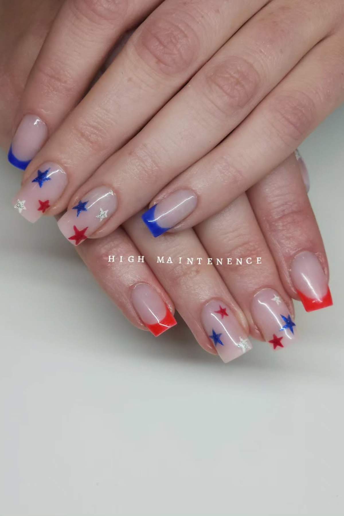 Close-up of hands with a French manicure in blue and red tips, decorated with red, blue, and silver star stickers on natural nails.