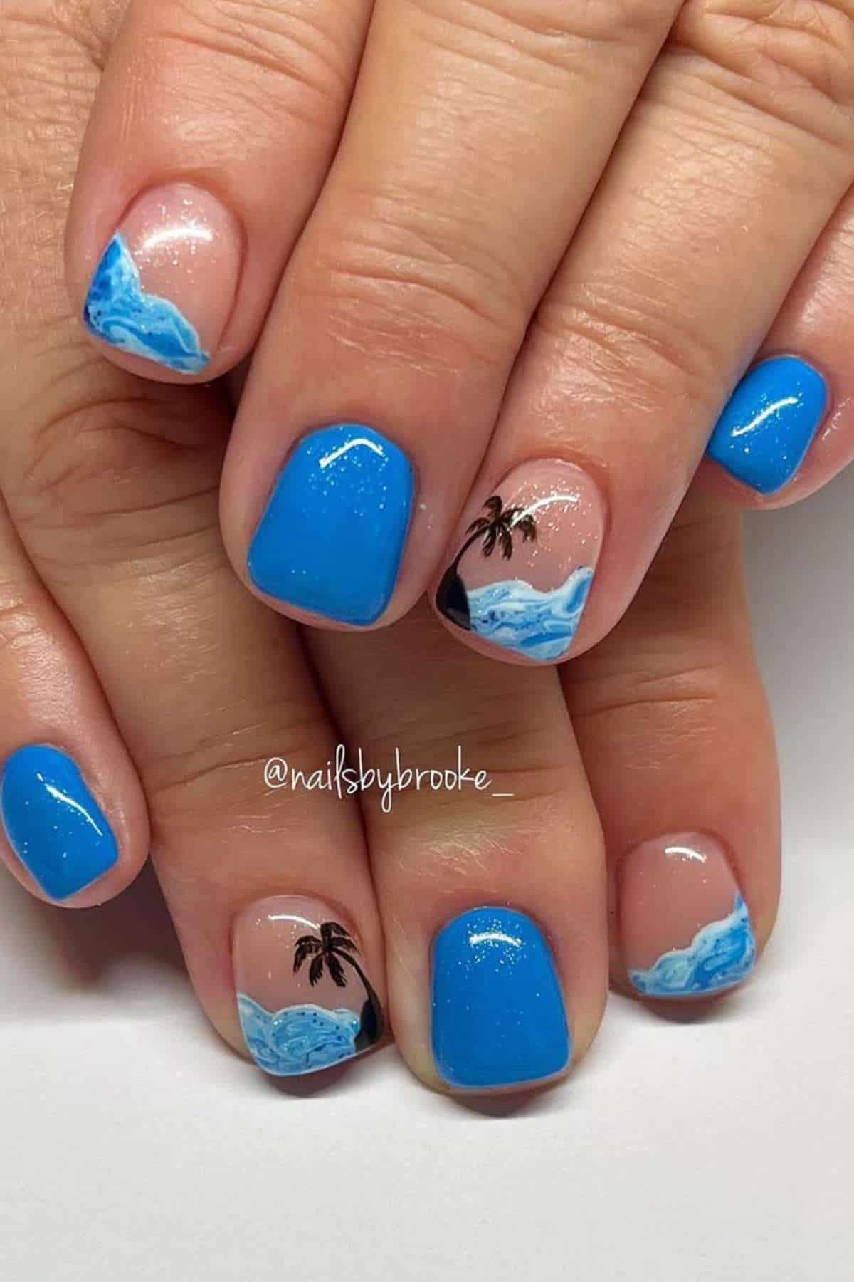 Fingernails painted with bright blue polish, featuring ocean wave designs and small black palm trees on a few nails.