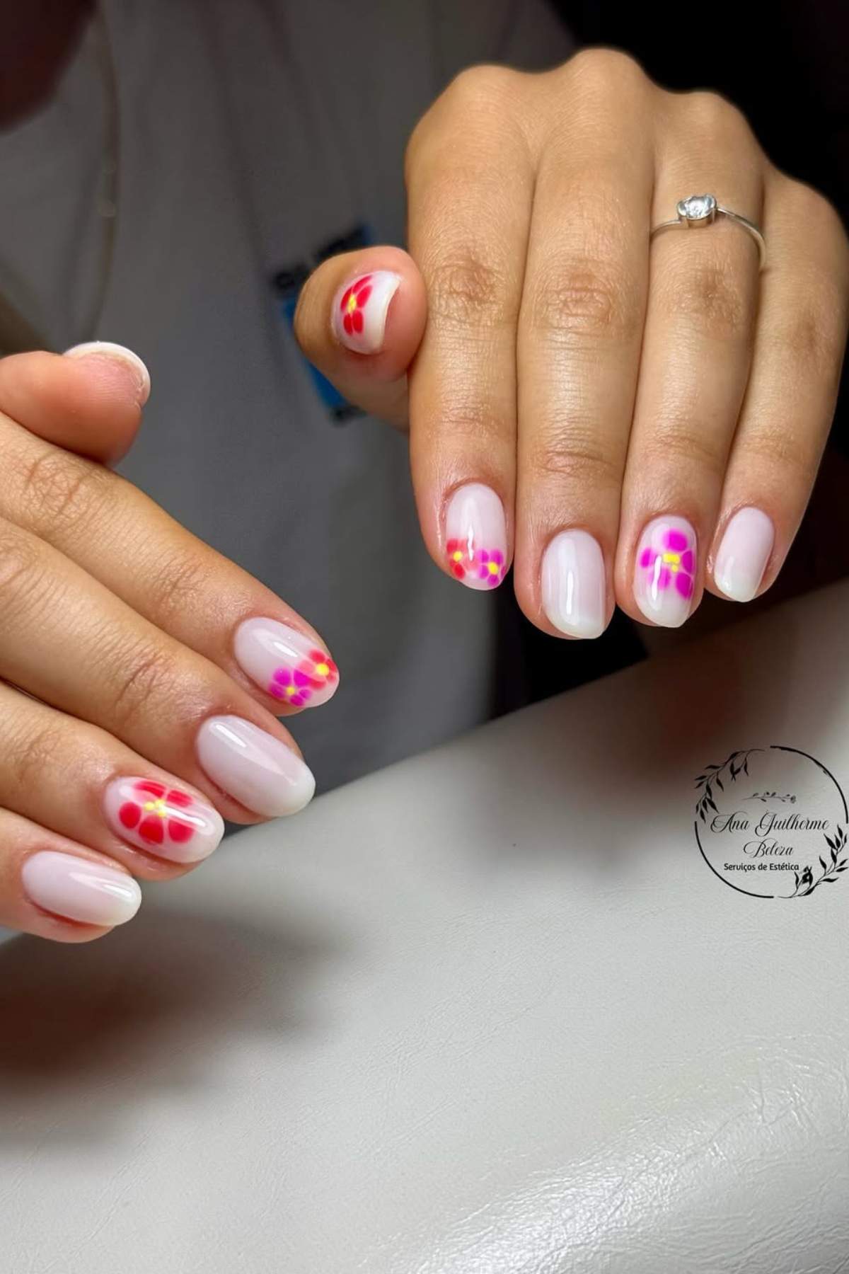 A hand with short, oval nails painted light pink, each nail decorated with a cluster of colorful dot designs near the tips.