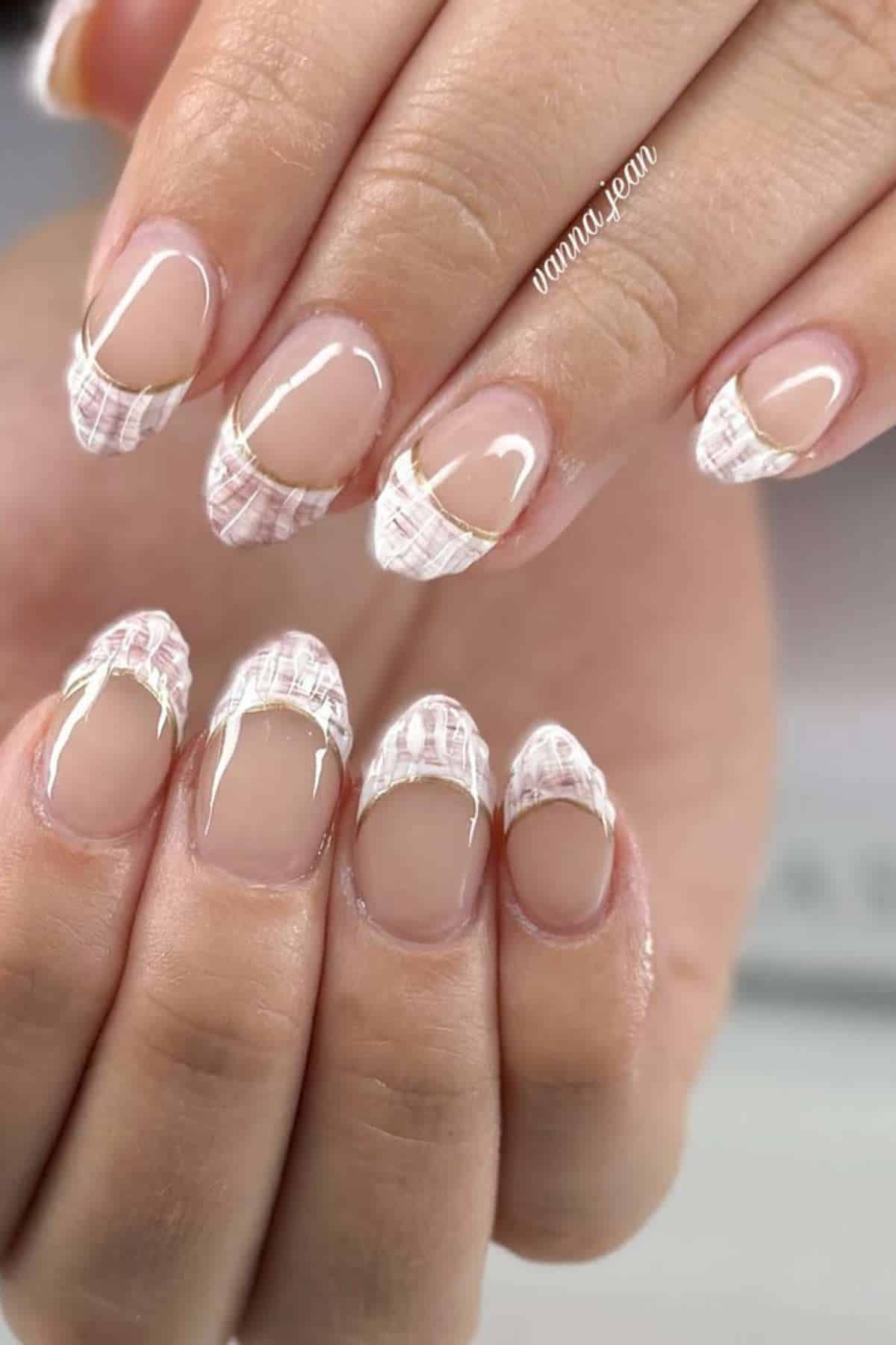 Hands with almond-shaped nails featuring a pink and white plaid French tip design and a gold accent line near the tips on a natural nude base.