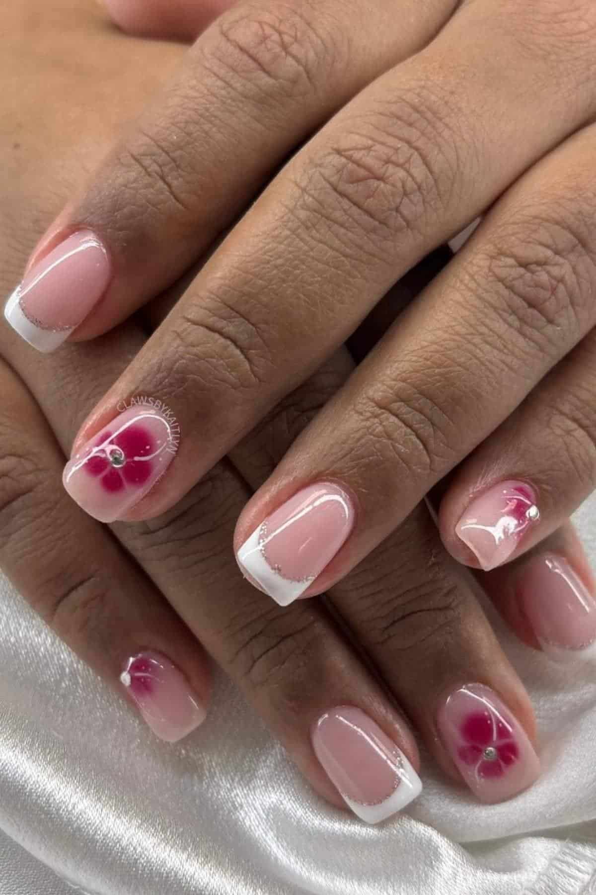 Close-up of hands with French tip manicure on short nails, featuring pink and white flower designs with small rhinestones on the ring fingers.