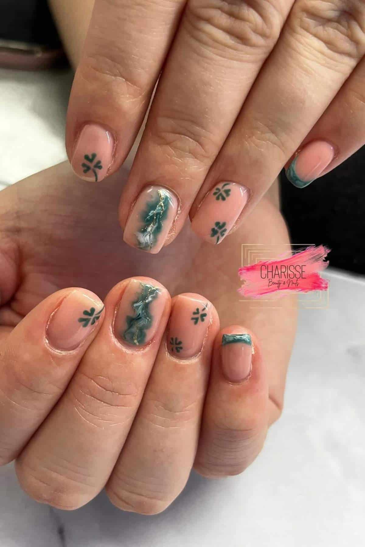 Hands with natural-colored nails featuring green abstract designs, small green clovers, and green French tips on some fingers.