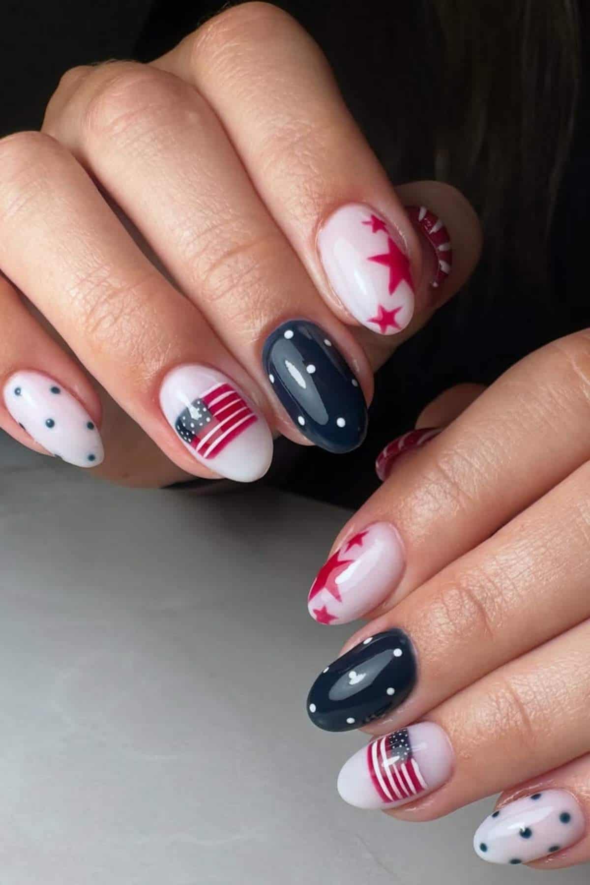 Close-up of hands with manicured nails featuring American flag designs, red stars, dark blue with white dots, and white with small blue dots.