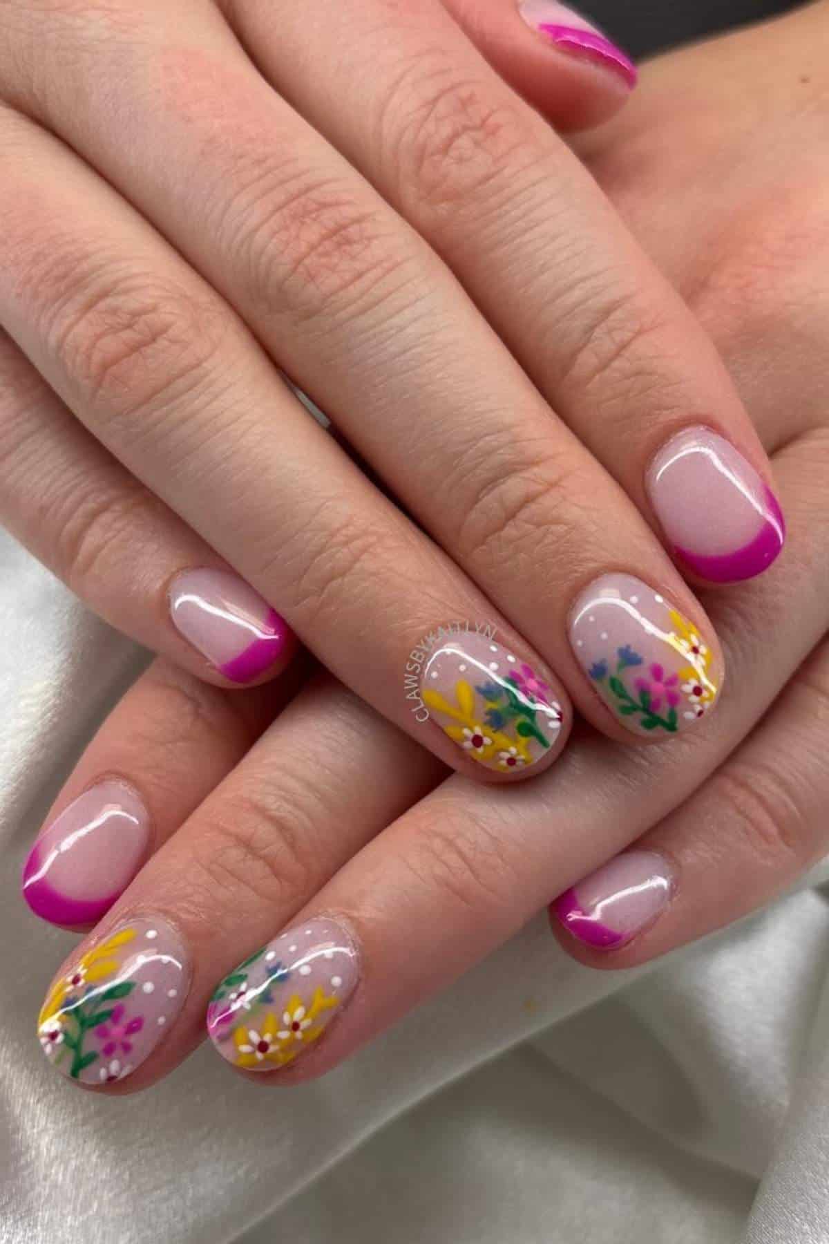 Hands with manicured nails featuring pink French tips and a floral design with yellow, pink, and green colors on a few accent nails.