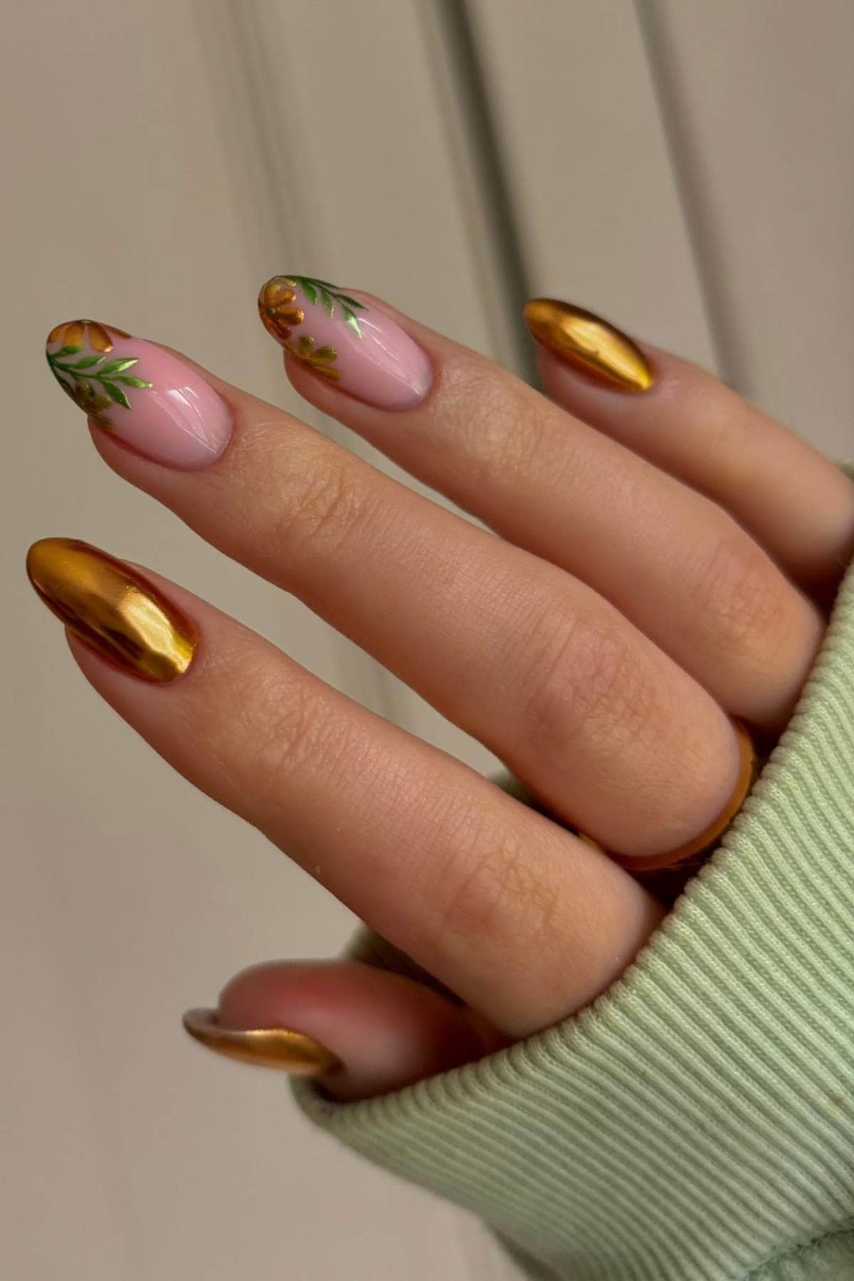A hand with gold metallic and pink floral nail art, wearing a light green ribbed sleeve.