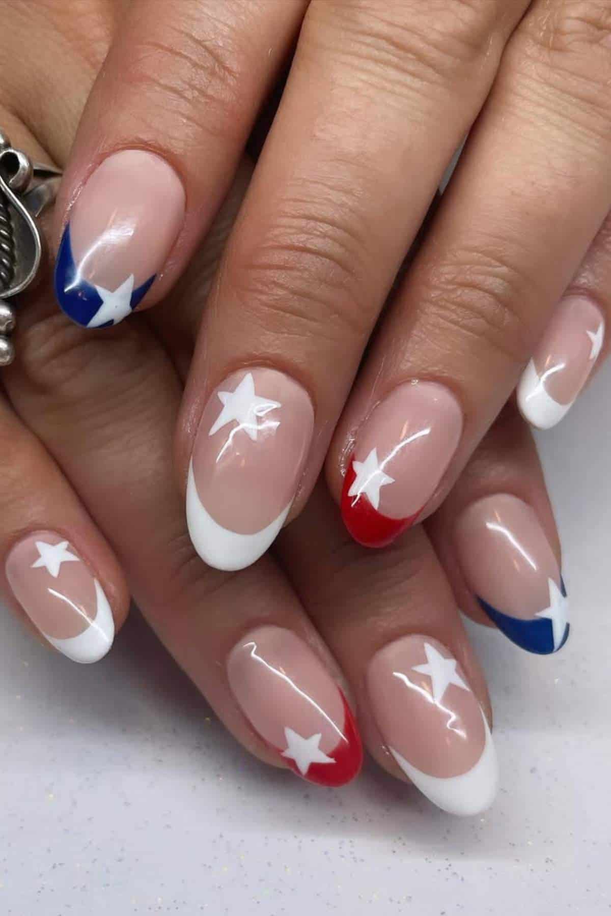 Close-up of hands with manicured nails featuring red, white, and blue tips and white star designs on a nude base.
