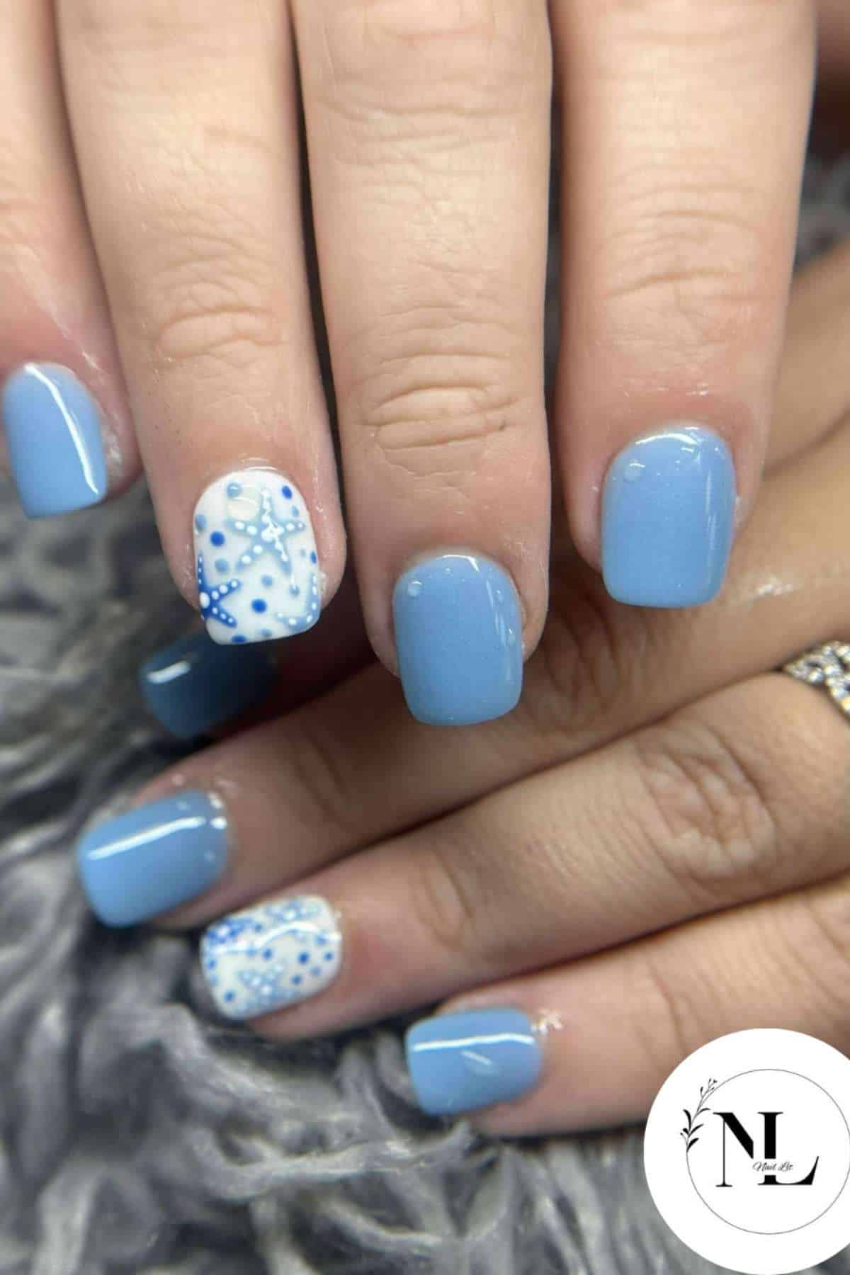 Hands with square-shaped nails painted light blue; ring fingers have white accent nails with blue and white dot and star-like designs.