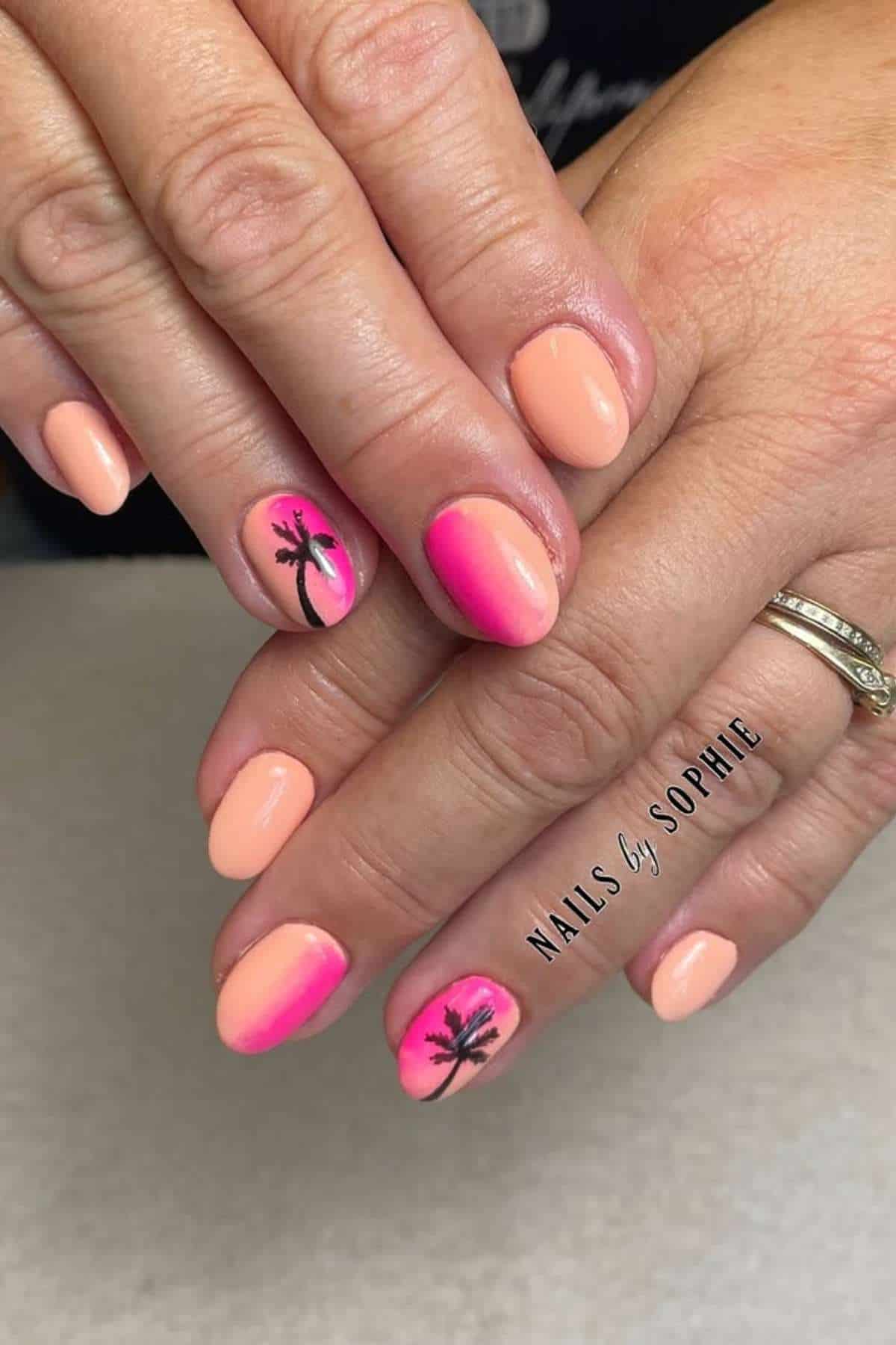 Hands with peach and pink ombre manicure; ring fingers feature black palm tree nail art. Nails are filed oval, and a silver ring is worn on one finger.