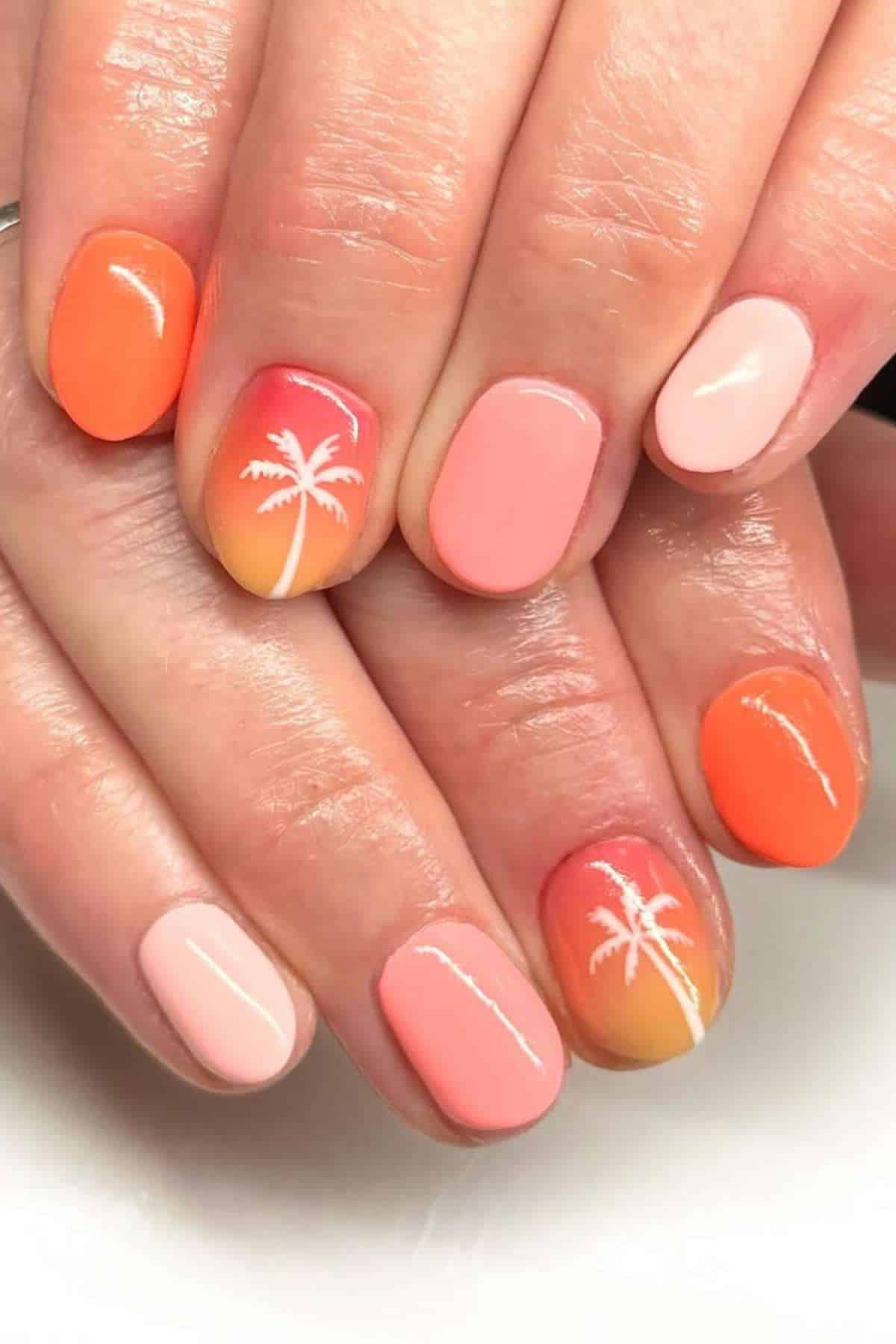 Hands with manicured nails featuring a pink and orange gradient, some with a white palm tree design, and others in solid coral or light pink polish.