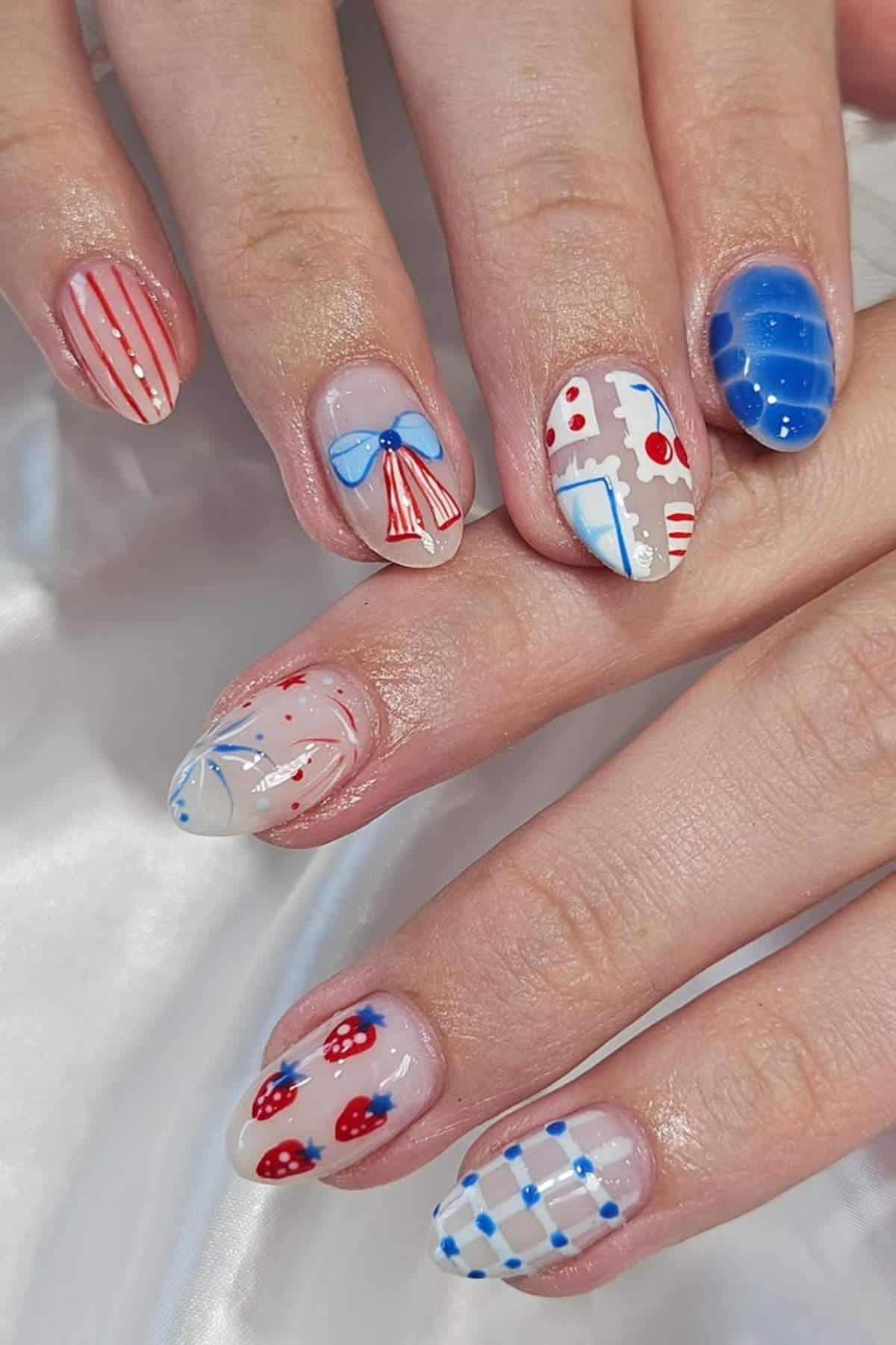 Fingernails with various colorful nail art designs, including stripes, polka dots, bows, hearts, and strawberries, painted in red, blue, and white tones.