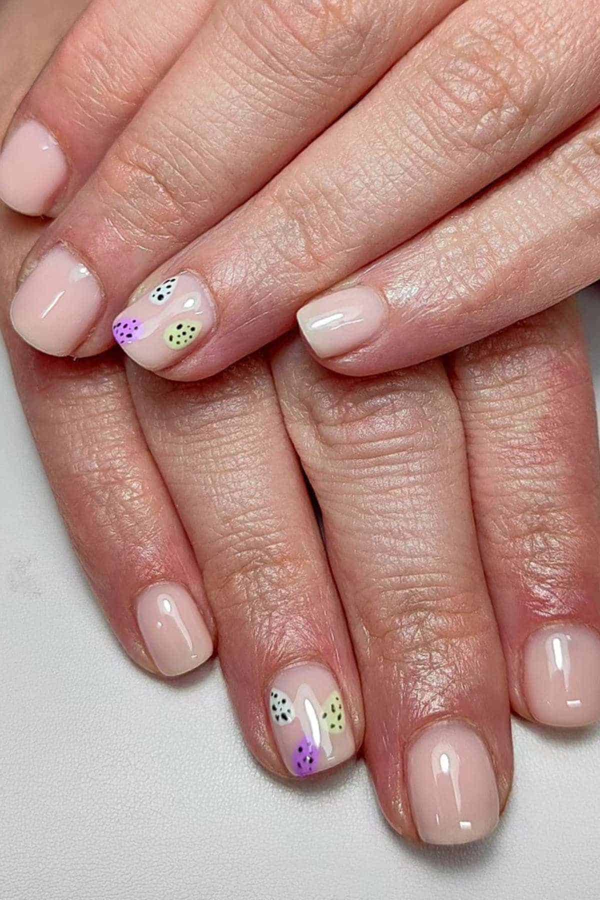 Hands with short, light pink manicured nails; accent nails feature colorful abstract leaf patterns with small black and white dots.