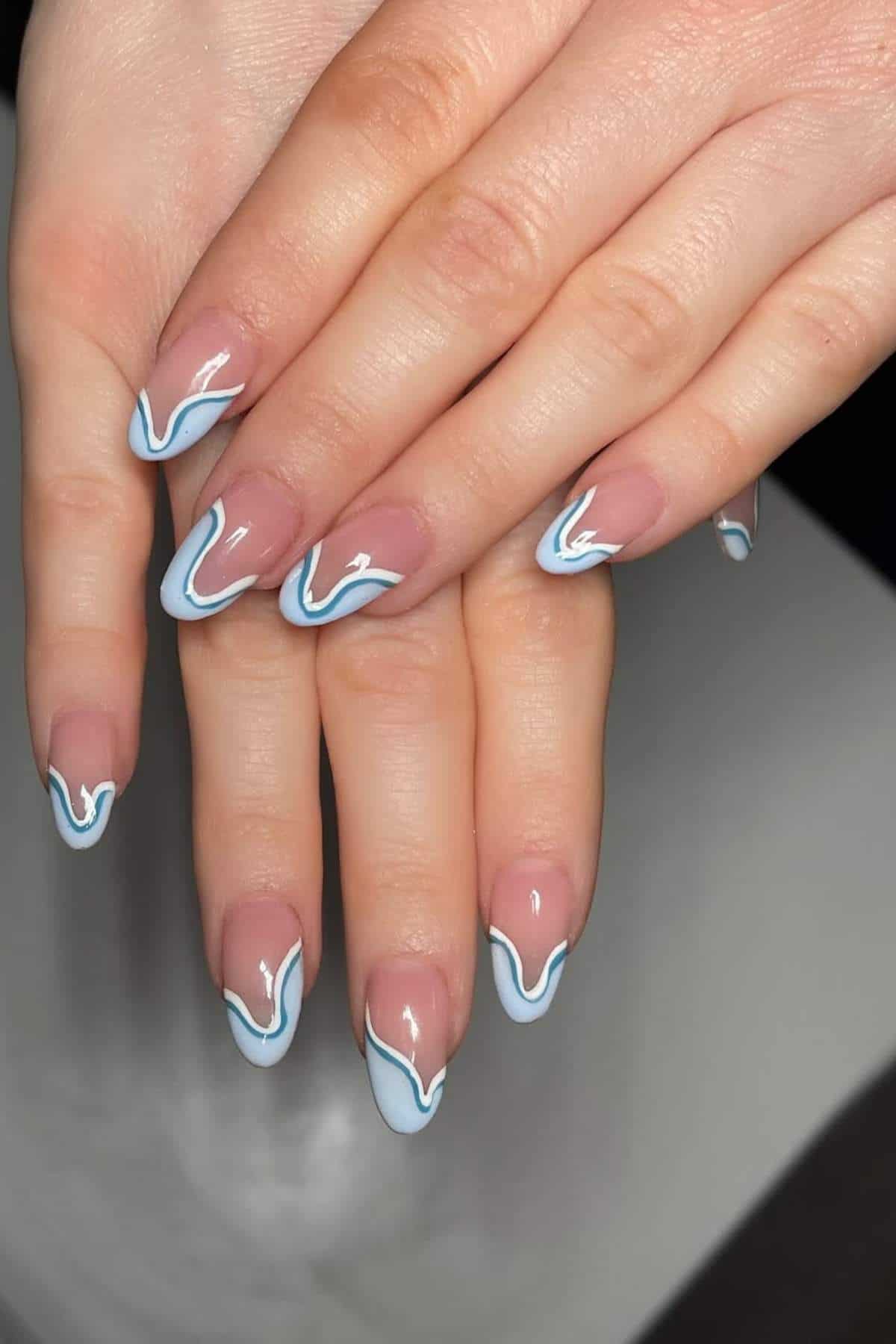 Hands with almond-shaped nails featuring a nude base and blue and white wavy line nail art.