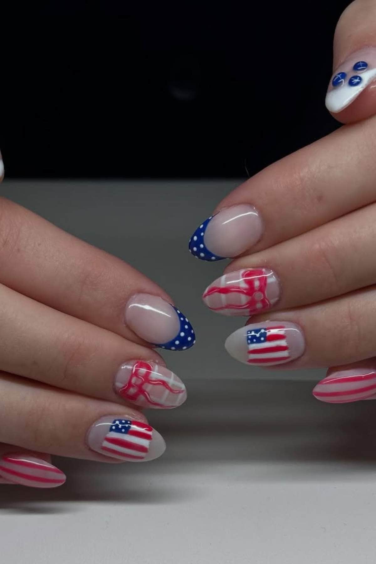 Hands with manicured nails featuring American flag designs and blue polka dots on some nails, against a plain background.