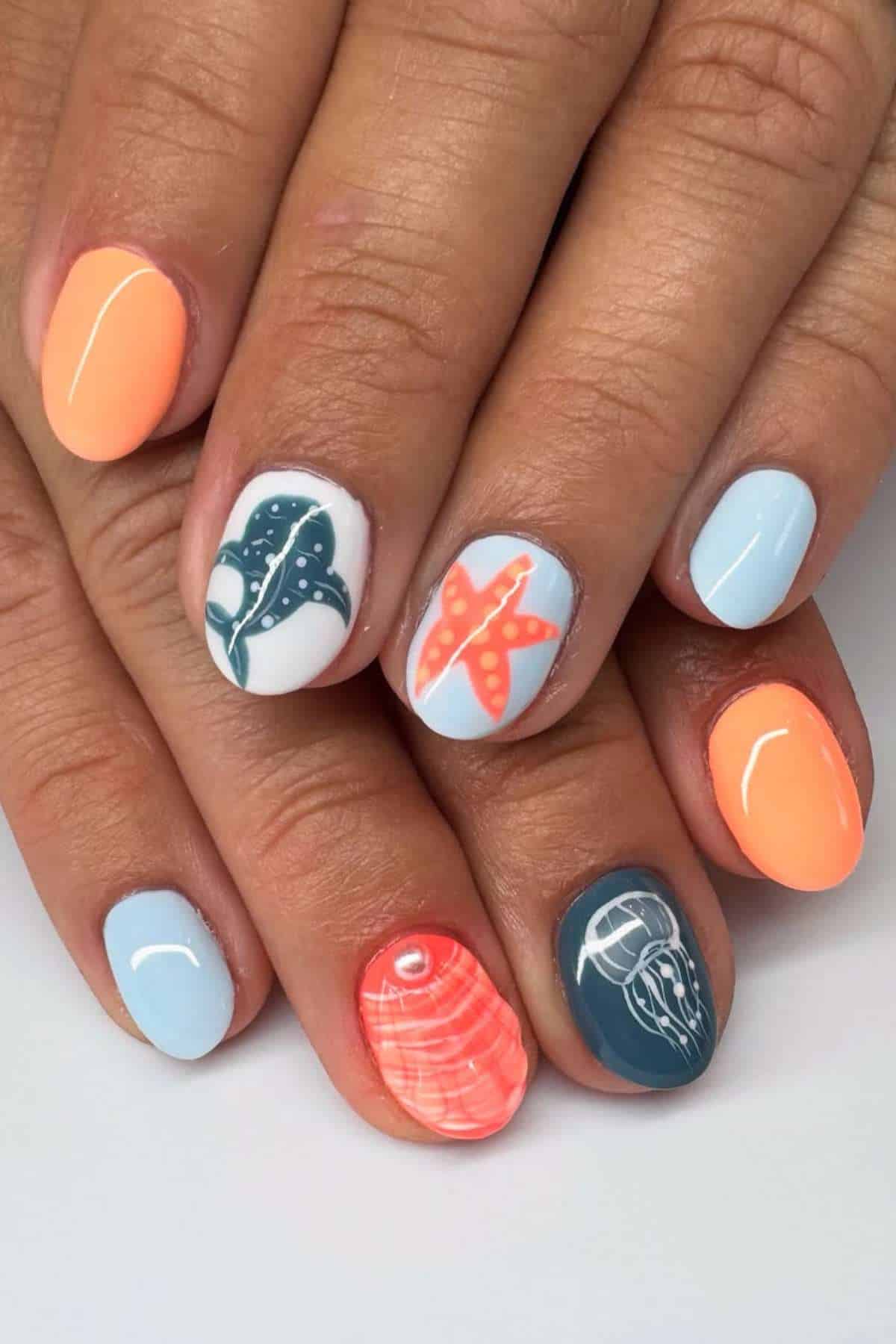 A hand with nails painted in pastel blue and orange, featuring marine-themed art including a stingray, starfish, shell, and jellyfish.