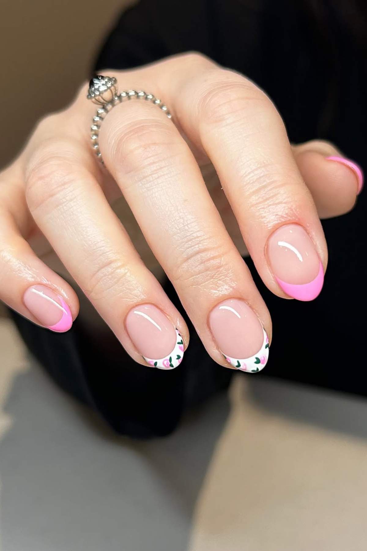 A hand with manicured nails featuring pink French tips and accent nails with a white base and small colorful dot patterns.