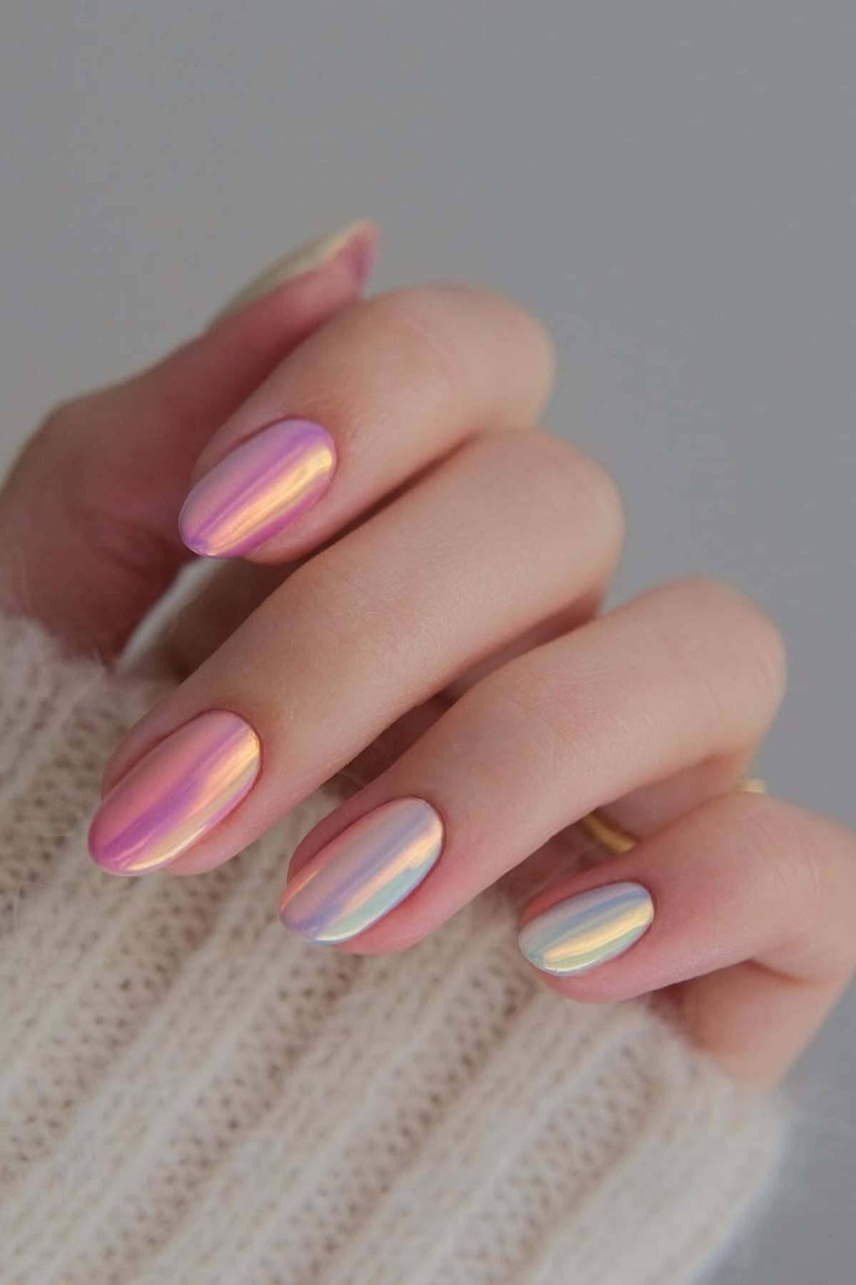 A hand with almond-shaped nails painted in a multicolored, iridescent chrome finish; the person is wearing a cream knit sweater.