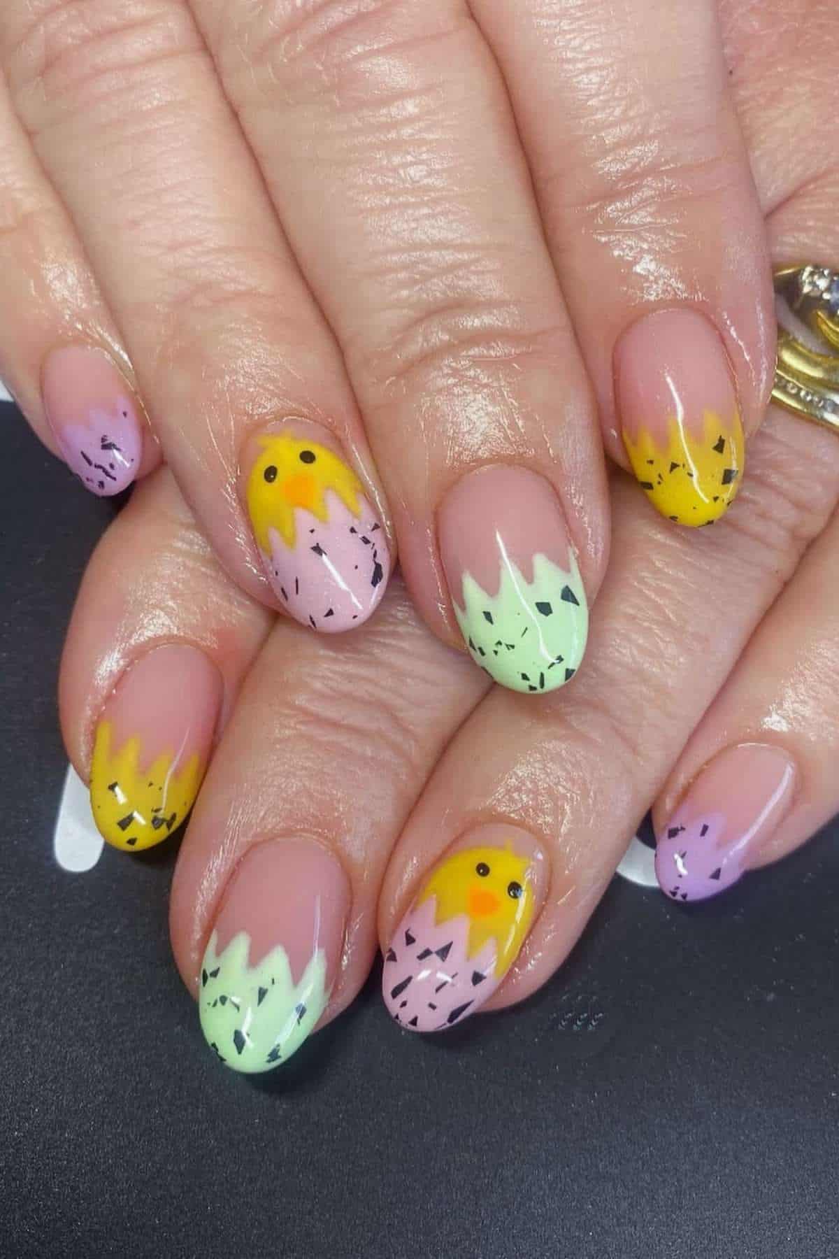 Fingernails with pastel-colored zigzag tips in yellow, green, and purple, black speckled accents, and small black dots on a neutral base.