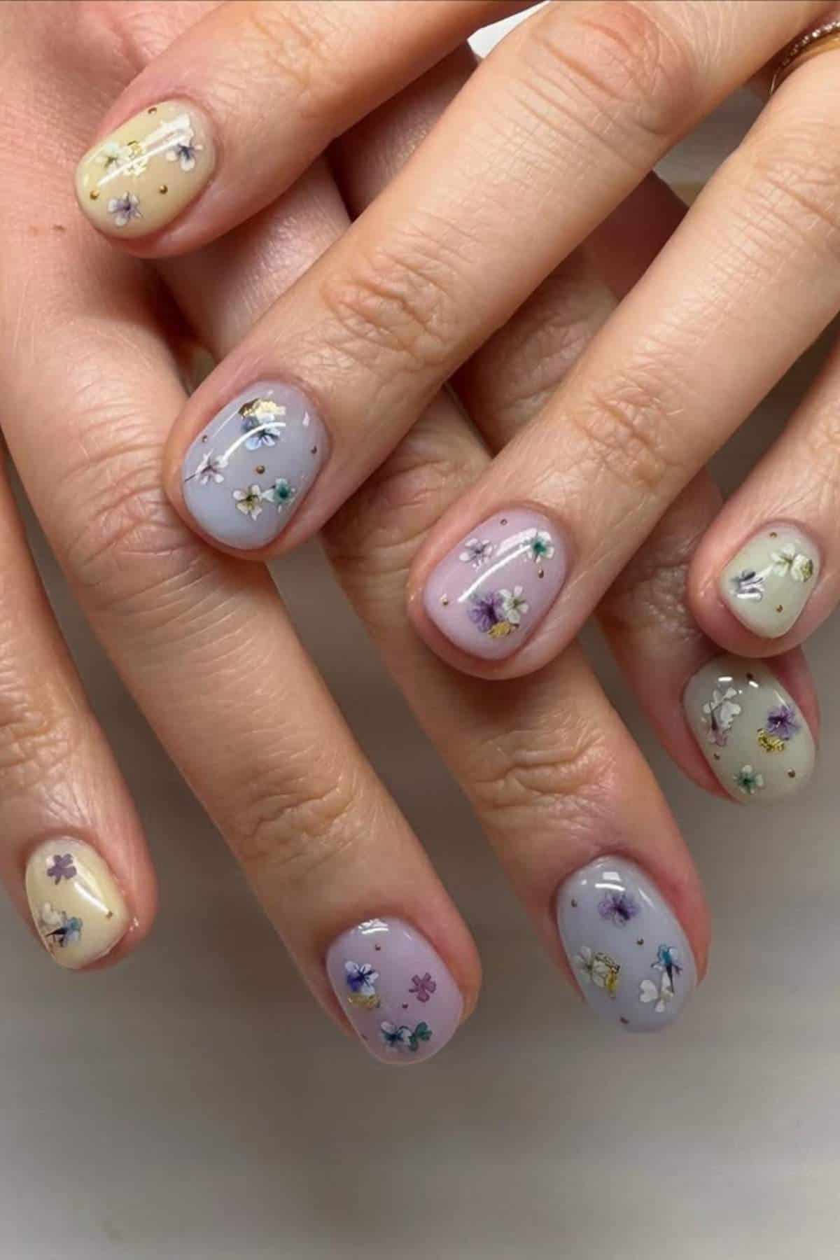 Close-up of hands with short nails painted in pastel colors and decorated with small, delicate floral designs.