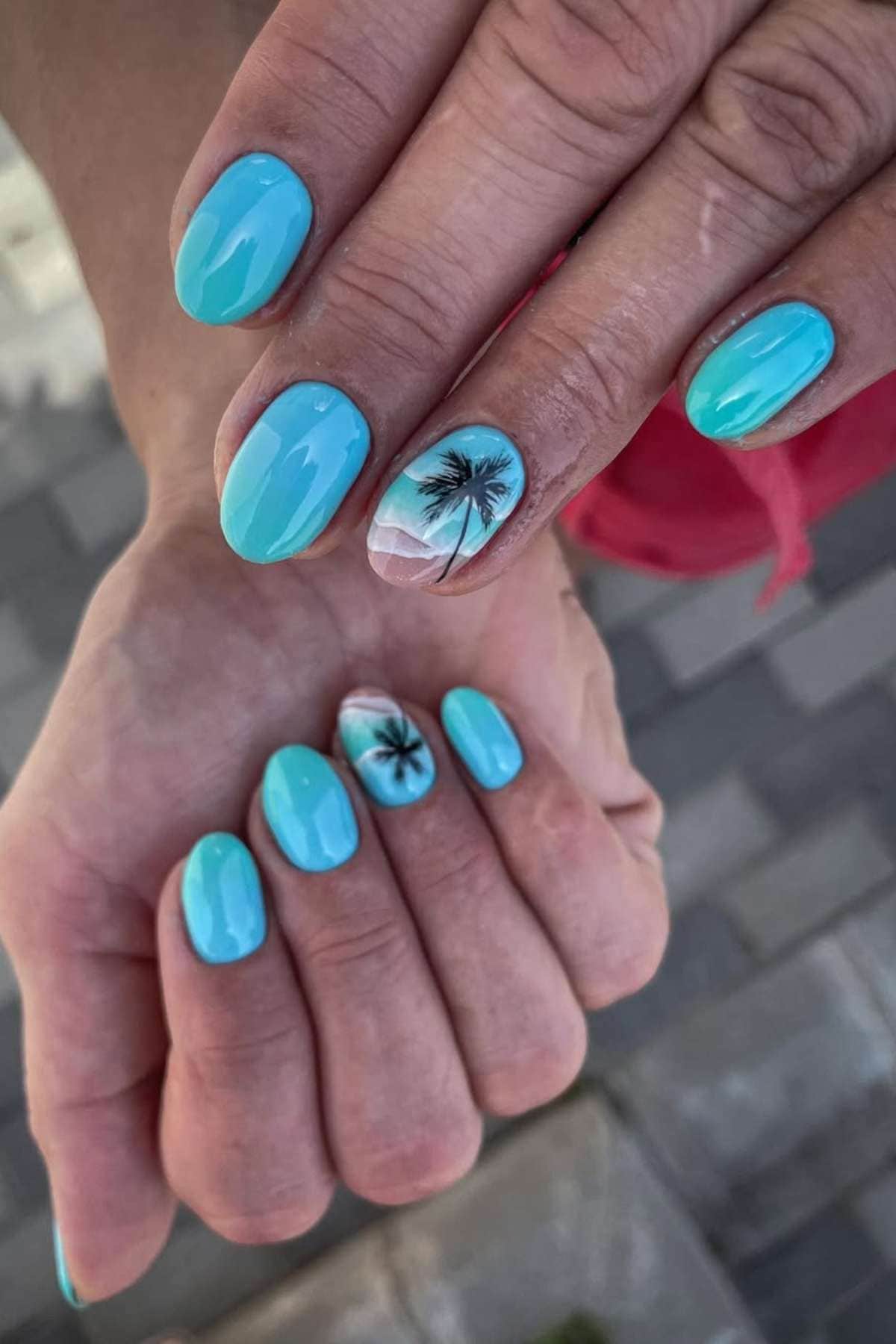 Hands with turquoise blue manicured nails; ring fingers feature accent nail art of a black palm tree on a gradient background.