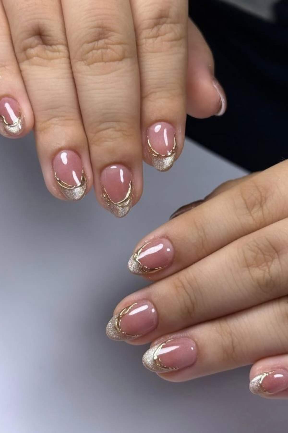 Hands with short, almond-shaped nails featuring a nude base and gold glitter French tip design.