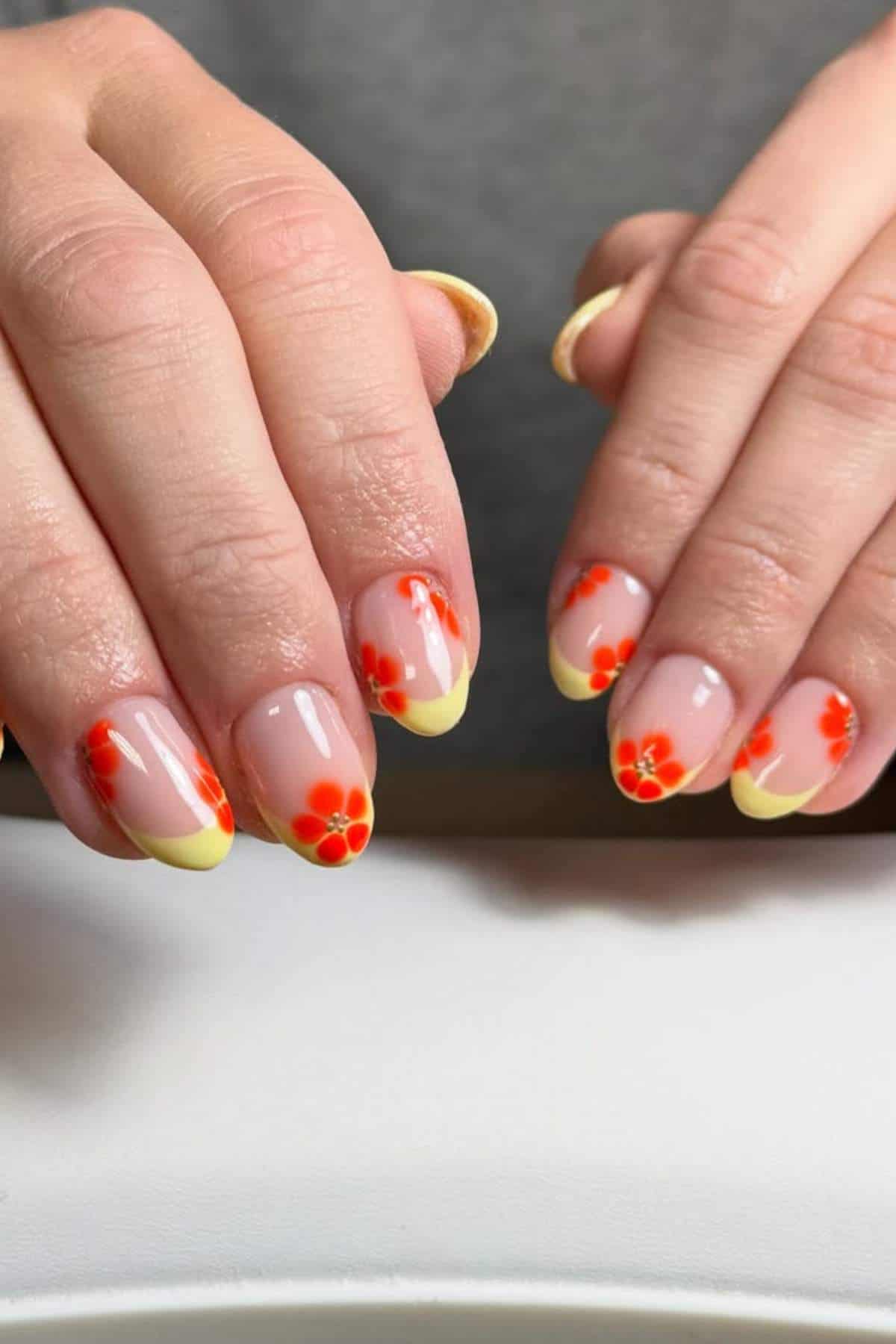Hands with a manicure featuring yellow French tips and small red and orange flower designs on natural-shaped nails.
