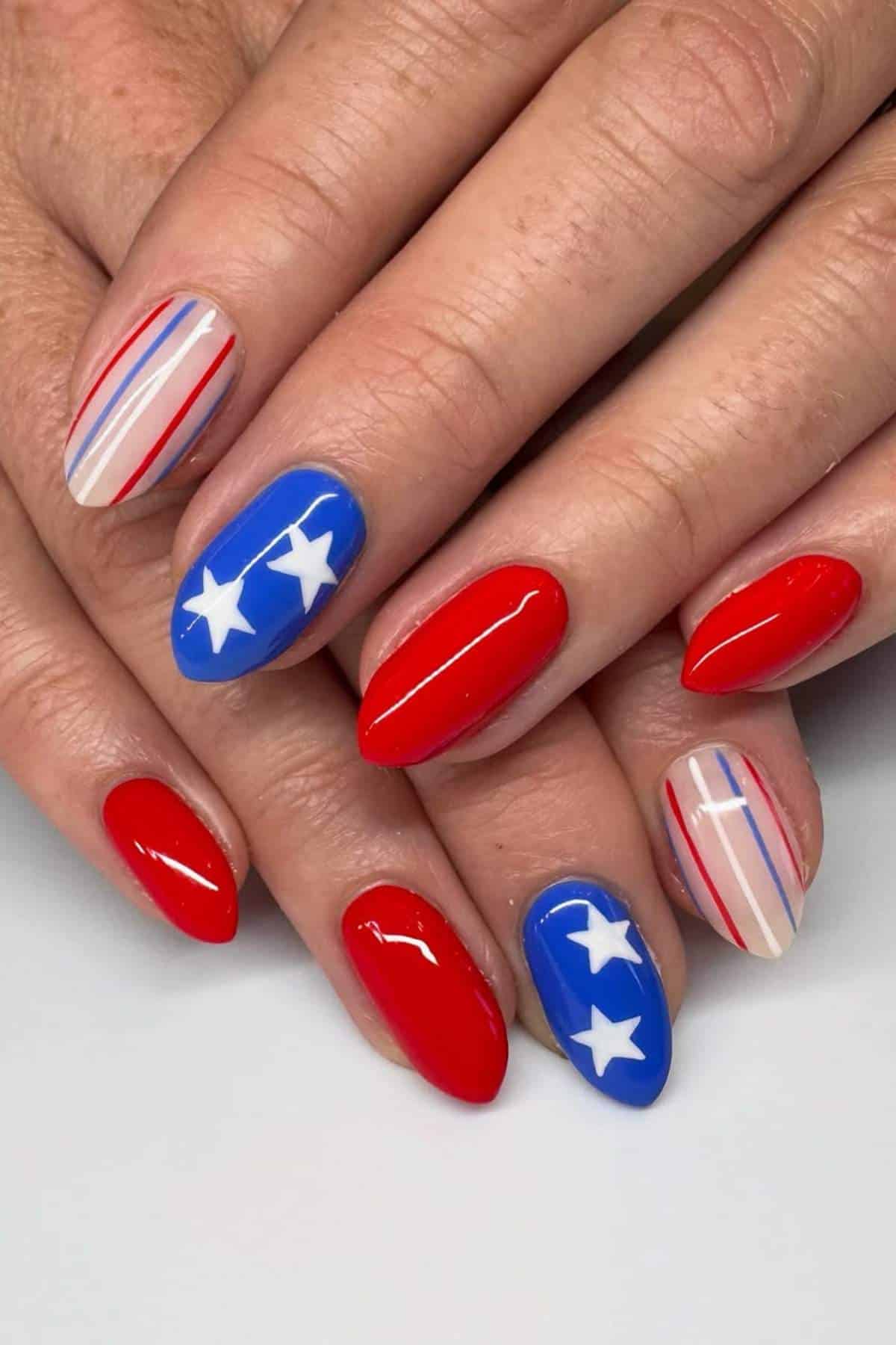 Hands with oval-shaped nails painted in a patriotic design featuring red, blue, and nude colors, white stars, and red and blue stripes.