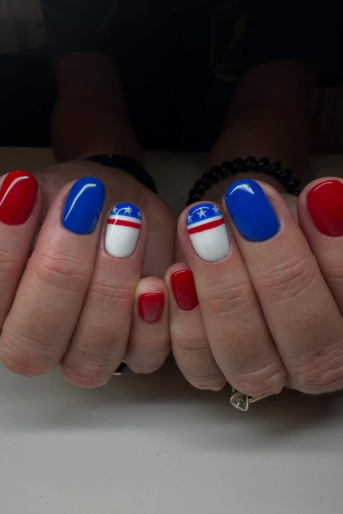 Hands with a patriotic manicure featuring red, white, and blue nails with star designs on the middle fingers.