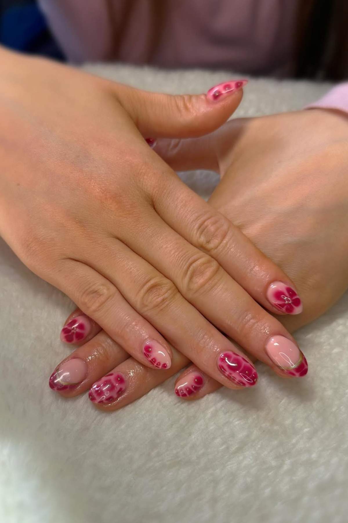 Hands with neatly manicured nails featuring pink and red floral designs on a light background, resting on a white surface.