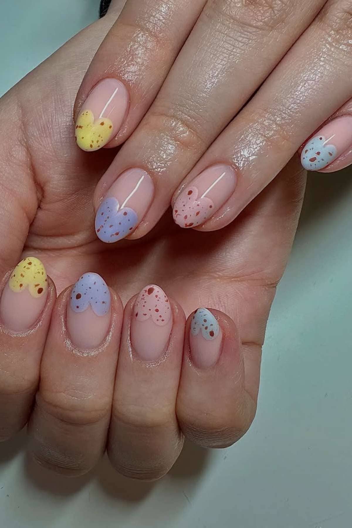 Hands with fingernails painted in pastel heart shapes at the tips, each heart decorated with small dots in matching colors.